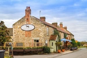 Charming stone inn with ivy-covered walls, chimney stacks, and outdoor seating under blue umbrellas on a country road.