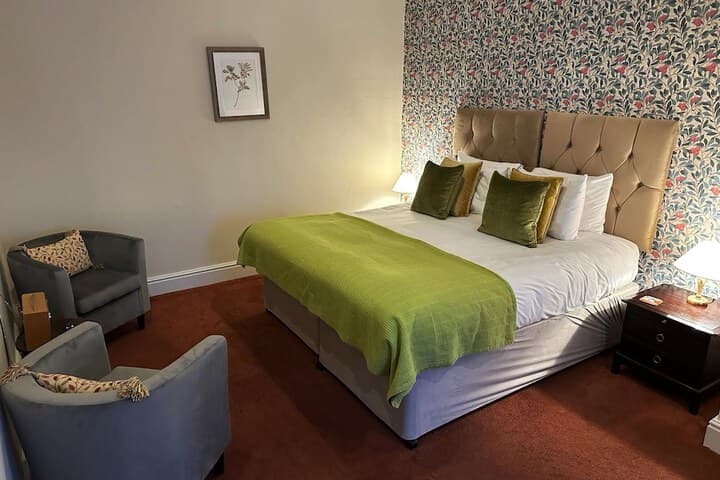 Elegant hotel room in Knaresborough with a floral accent wall, plush bed, green throw, and cozy seating area.