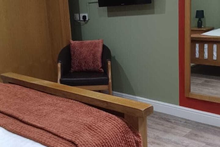 Cozy hotel room with a wooden bed, red accents, green walls, and a wall-mounted TV in Mosborough, Yorkshire.