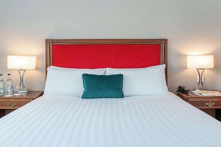 Elegant hotel room in Ilkley with a plush red headboard, crisp white bedding, bedside lamps, and a teal cushion.