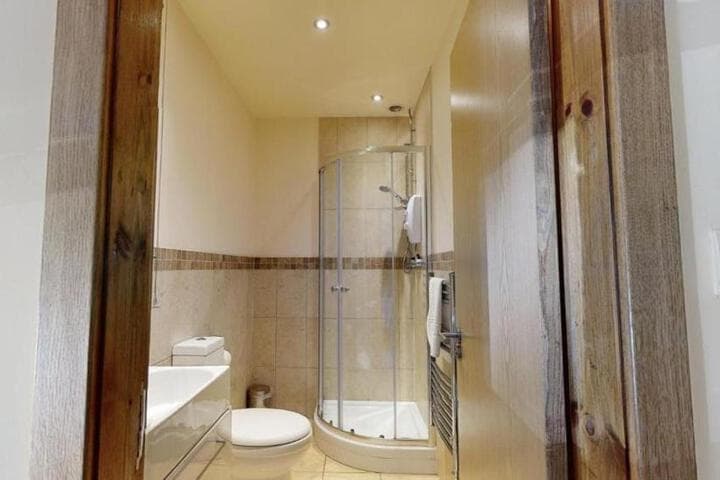 Cozy bathroom in The Horse & Farrier, Otley, features tiled walls, a glass shower, wooden door, and modern fixtures.