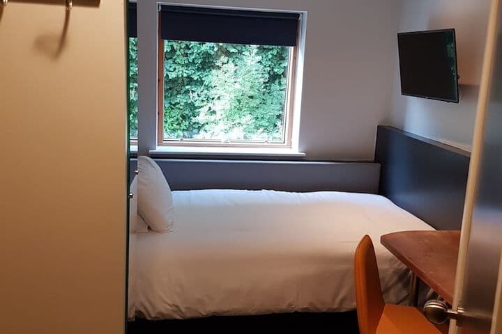 Cozy hotel room with a single bed, orange chair, and TV, overlooking lush green trees through a window in Ecclesall, Yorkshire.