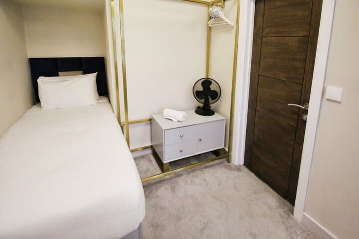 Single bed room at The Psalter, Nether Edge, with beige walls, wooden door, small fan, and light grey furnishings.