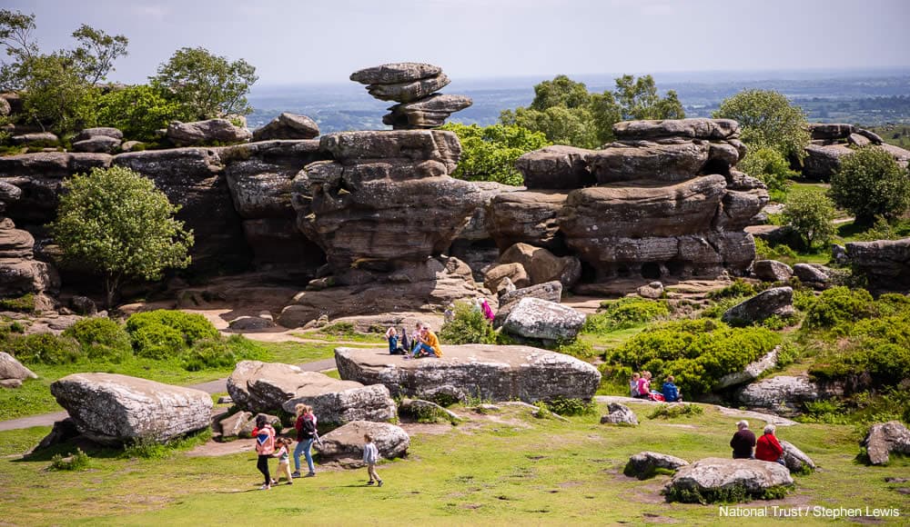 Dramatic sandstone rock formations surrounded by greenery, with people exploring and relaxing on the stones.
