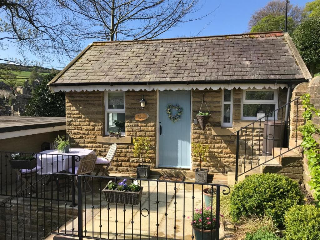 Charming stone cottage with a blue door, flower wreath, patio table, and garden under a clear blue sky.