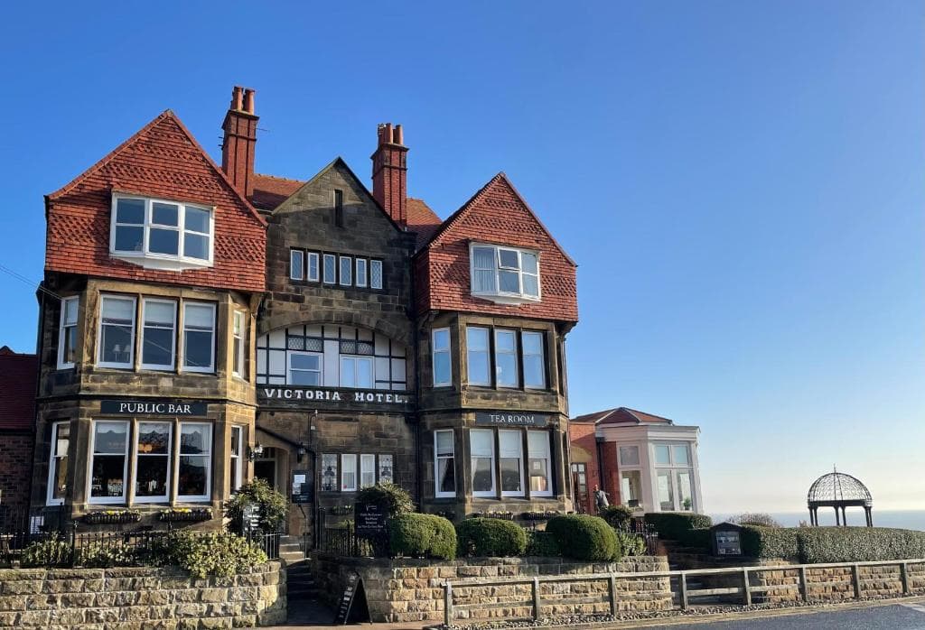 Victorian hotel with red gabled roofs, large windows, and manicured shrubs under a clear blue sky.