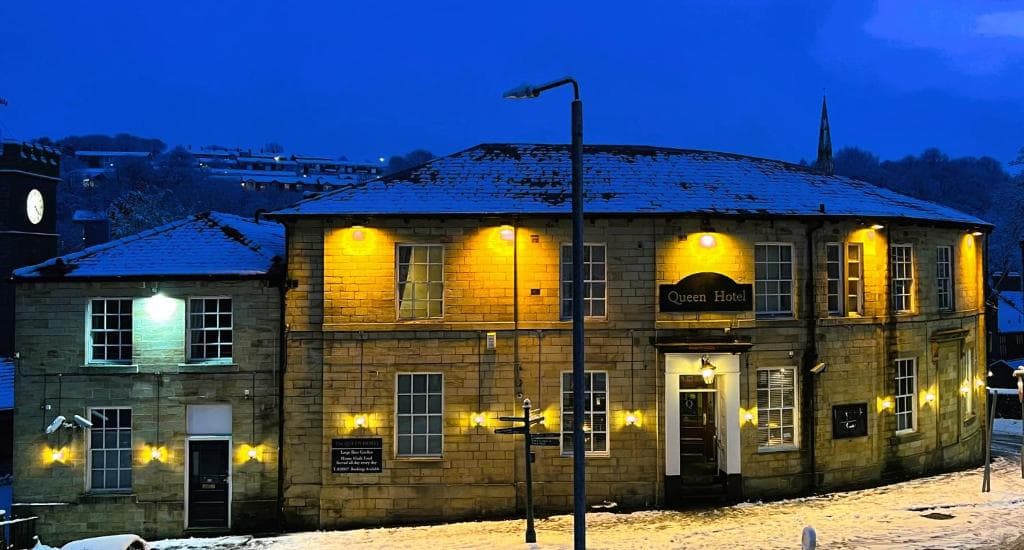 Historic stone hotel with warm lights, snow-dusted roof, and surrounding winter landscape at dusk.