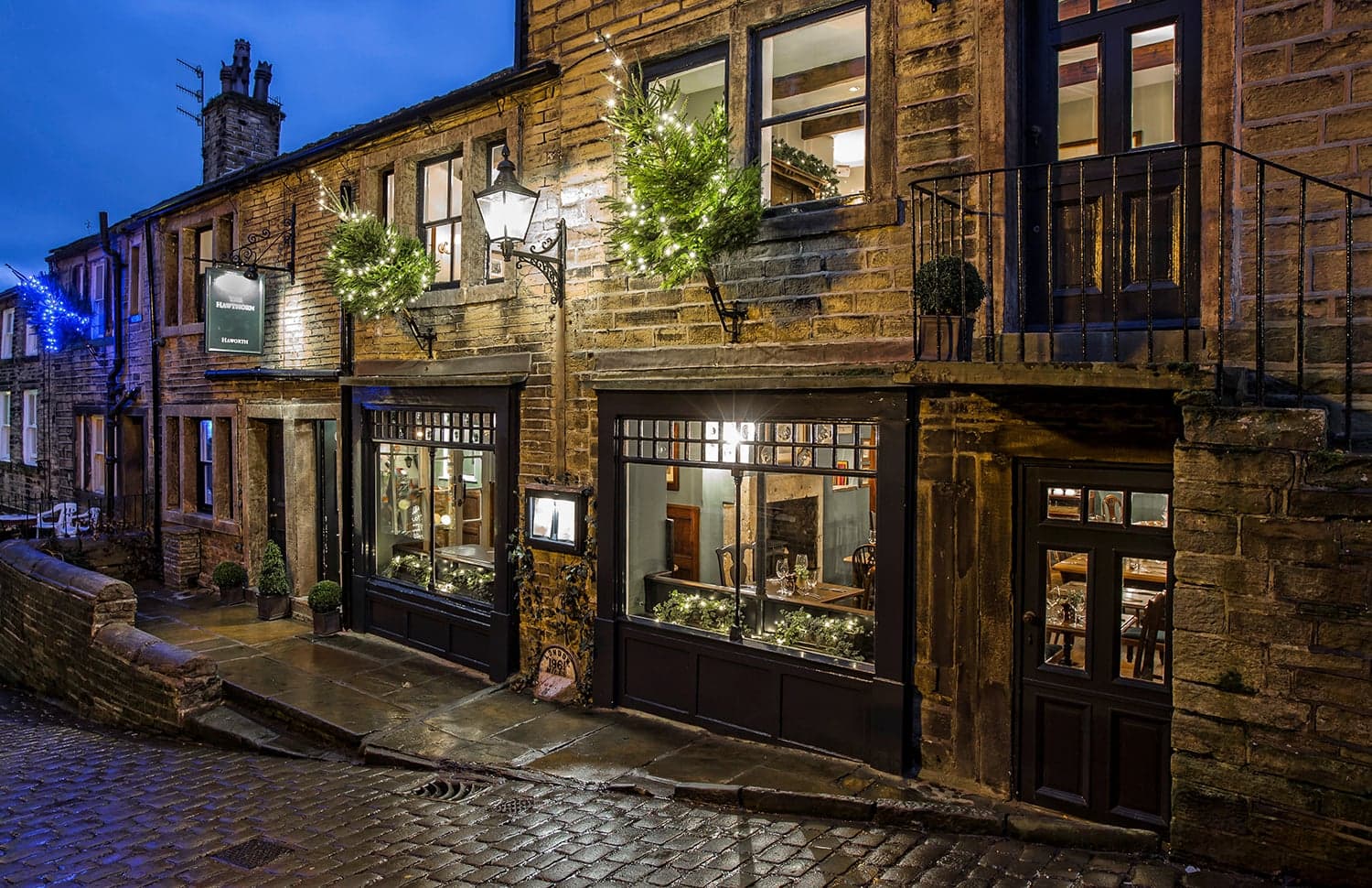 Historic stone building with festive lights, large windows revealing a cozy restaurant interior on a cobblestone street.