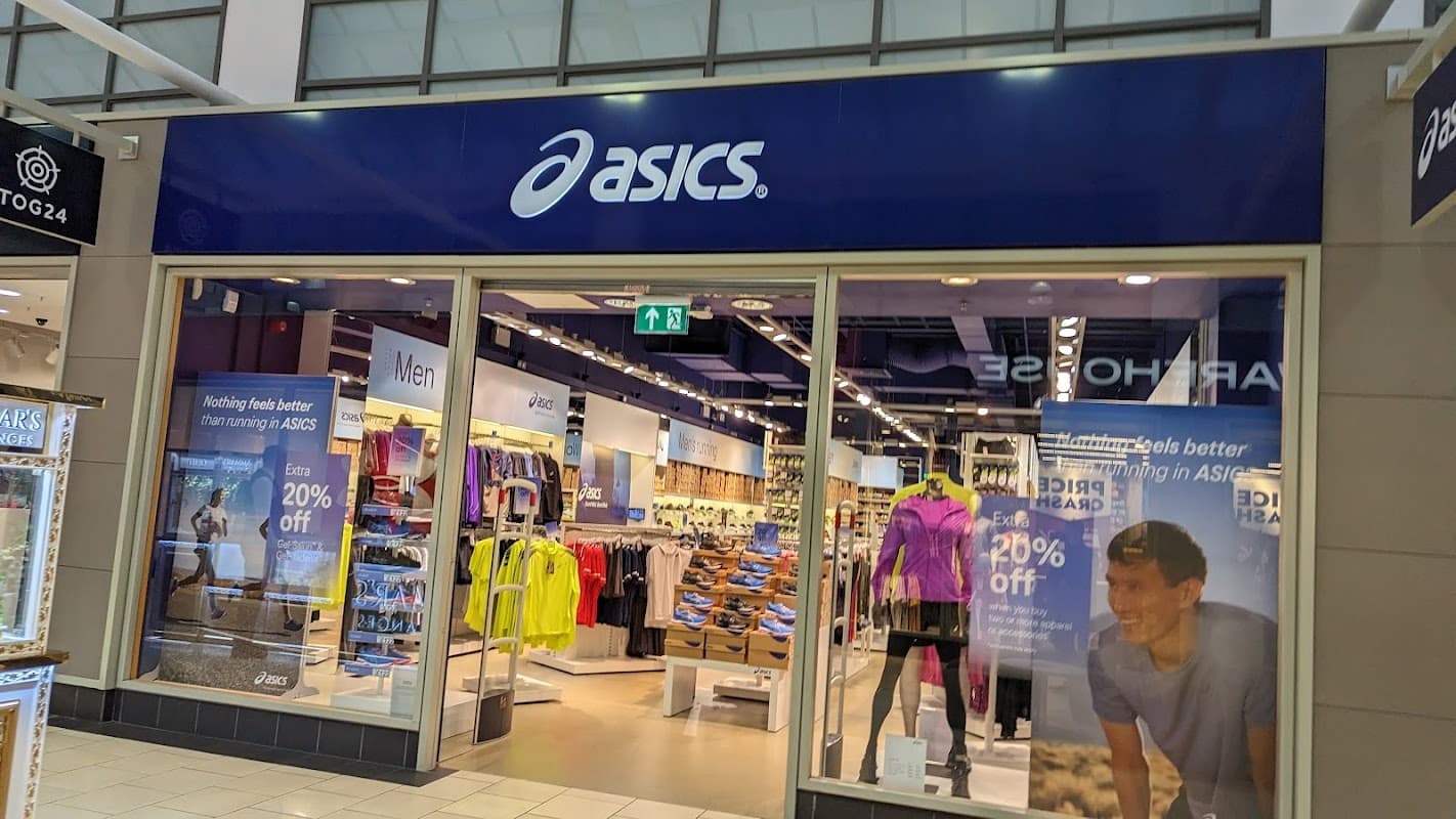 ASICS store front in a shopping center, featuring sports apparel and footwear, with promotional signage visible.