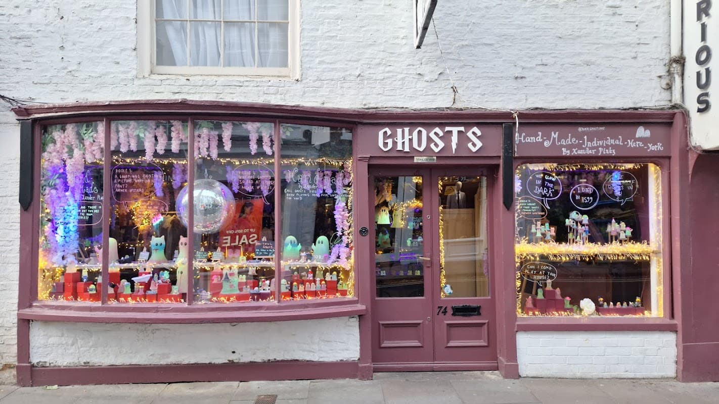Colorful shop window with whimsical decorations, ghost figures, and bright lights, showcasing handmade gifts for sale.