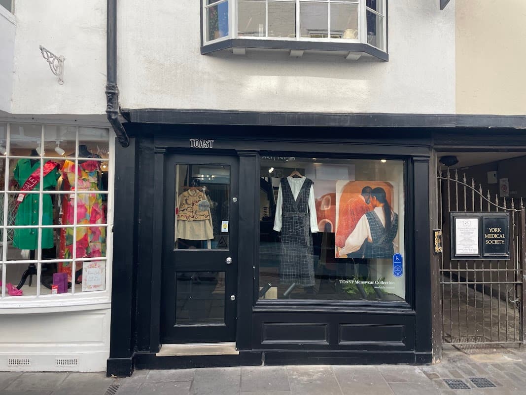 Black storefront of TOAST with clothing displays, including a dress and a patterned top, next to a colorful window display.