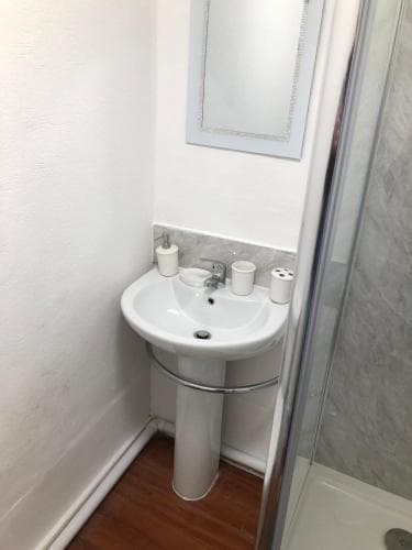 Compact bathroom with a white pedestal sink, wall mirror, and shower, featuring minimalist decor at Wellington Tavern, Dewsbury.