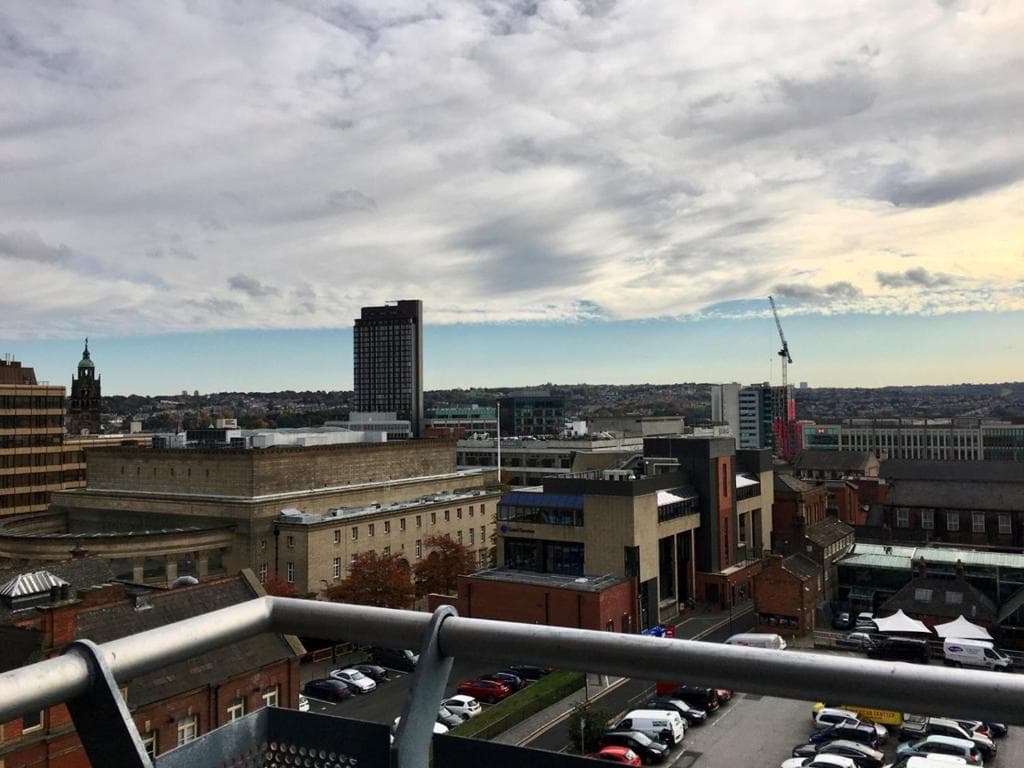 Skyline view of Sheffield city center with modern and historic buildings under a cloudy sky, seen from a rooftop.