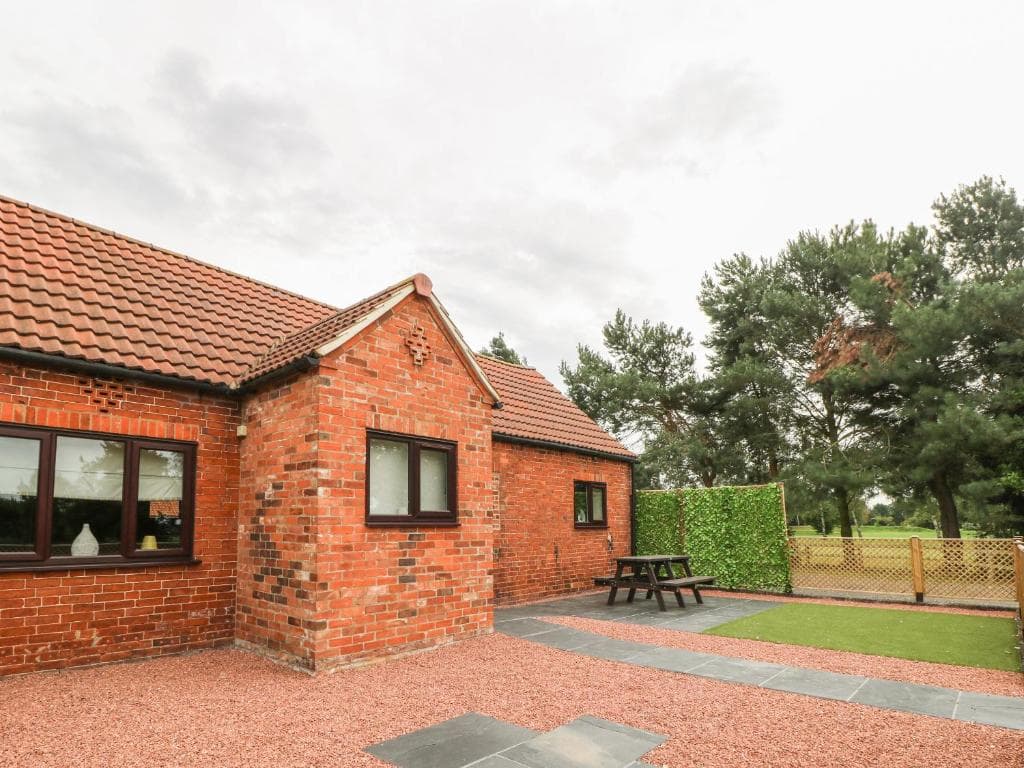 Red-brick cottage with red-tiled roof, surrounded by trees and gravel path, in The Stable, York, Escrick.