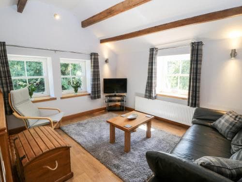 Cozy Bull Hill Cottage living room in Keighley, featuring beams, plaid curtains, and woodland views through large windows.