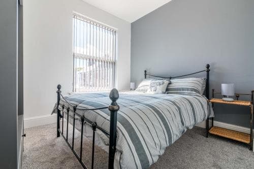 Bright bedroom with a striped bedspread, black metal bed frame, gray walls, and sunlight streaming through a window in Hull.
