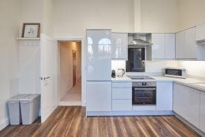 Modern kitchen in South Cliff Apartment, Scarborough, featuring sleek white cabinets, stainless steel appliances, and wood flooring.