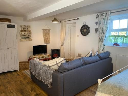 Cozy living area in Grinkle Bell Cottage, Yorkshire; features a grey sofa, rustic decor, wooden floor, and a small window.