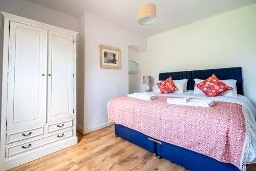 Bright hotel room with a large bed, floral cushions, a pink throw, white wardrobe, and wooden floor in York.