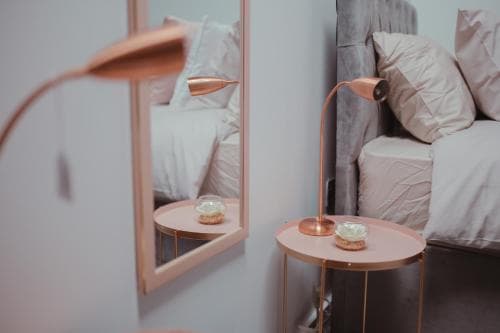 Elegant bedroom in Bradford penthouse with plush bed, pink side table, copper lamp, and mirror reflection.