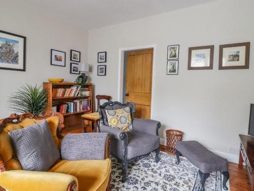 Cozy living room in 5 East Street, Bell Busk, Yorkshire, with vintage chairs, bookshelves, framed art, and a patterned rug.