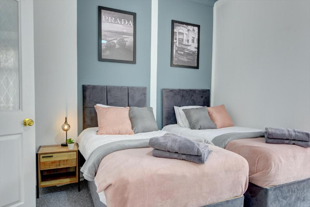 Twin beds with pink blankets and gray headboards, framed art, and a wooden nightstand in a cozy Hull apartment.