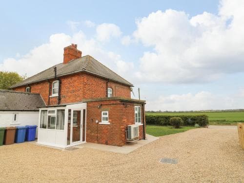 Red brick cottage in Hull, Yorkshire, with a gravel driveway, surrounded by green fields under a partly cloudy sky.