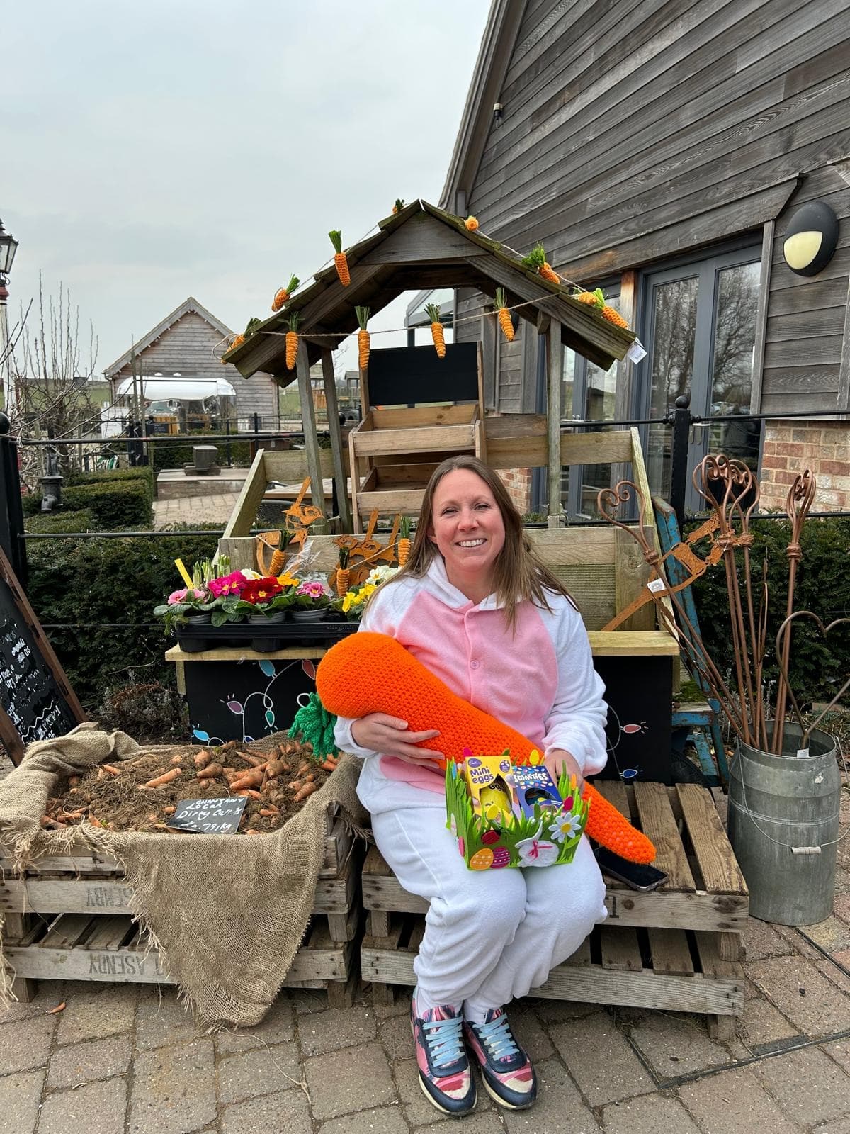 A woman in a bunny costume sits on a wooden cart decorated with carrots, surrounded by greenery at Pickering farm shop.