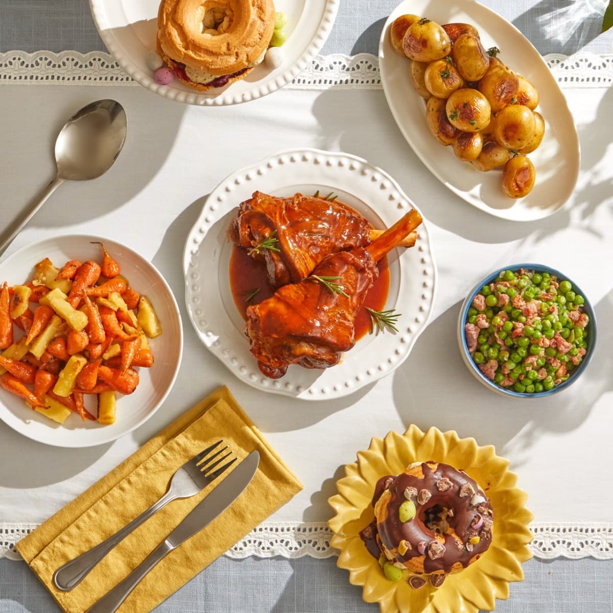 A beautifully arranged Easter feast featuring glazed lamb, roasted vegetables, and sweet treats on a festive table setting.