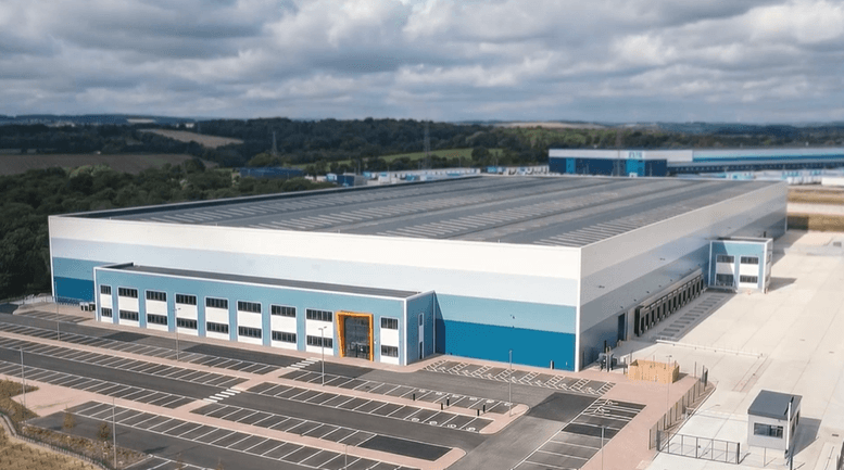Aerial view of Evri's new Barnsley hub, showcasing a large, modern warehouse with a blue and white exterior against a cloudy sky.