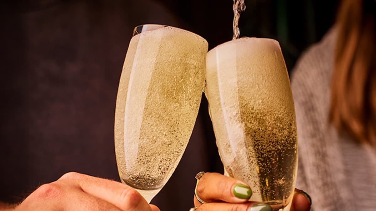 Two glasses of sparkling wine clink together, capturing a celebratory moment with bubbles rising in a cozy setting.