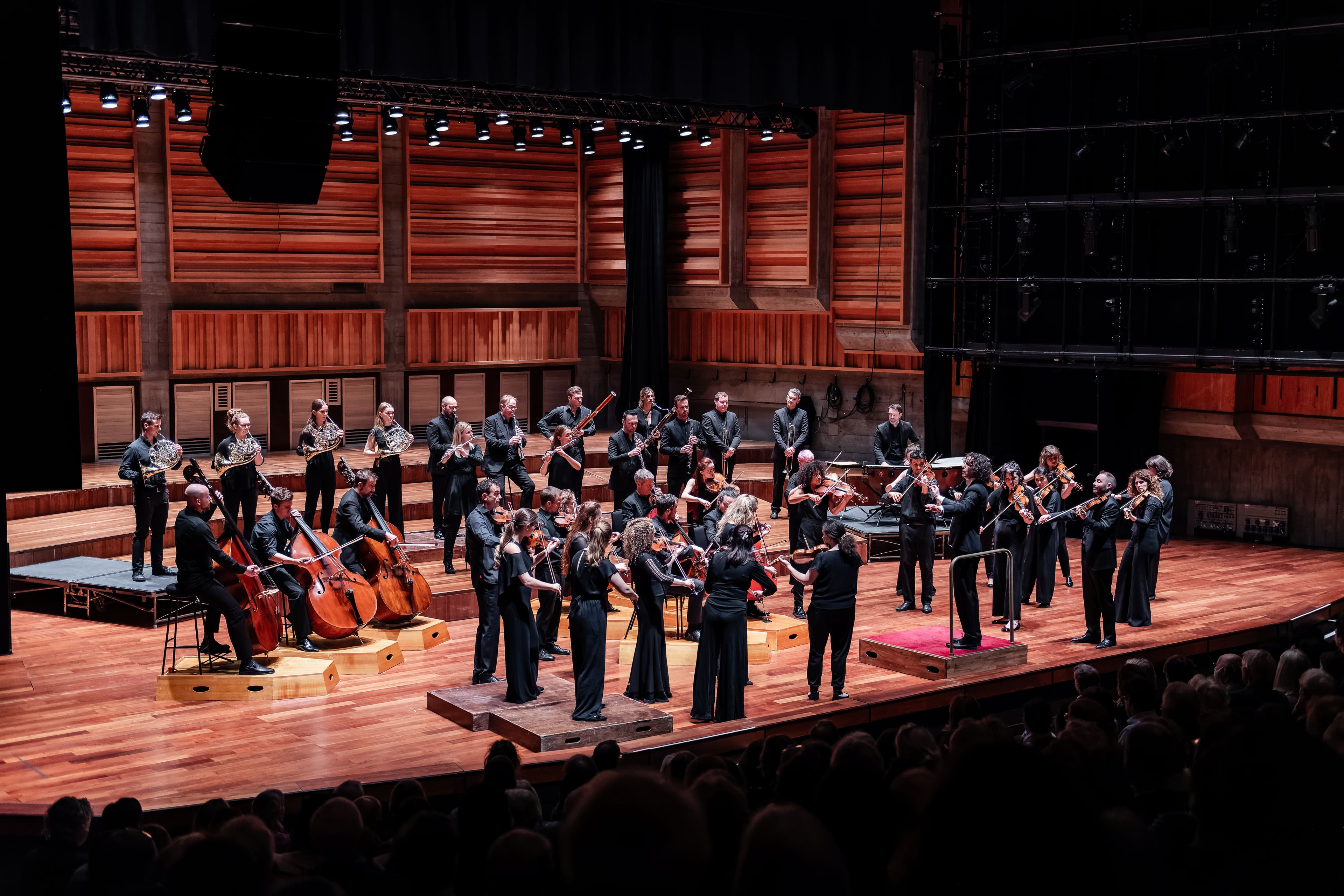 A vibrant orchestra performs on stage in a modern concert hall, surrounded by an engaged audience in Harrogate.