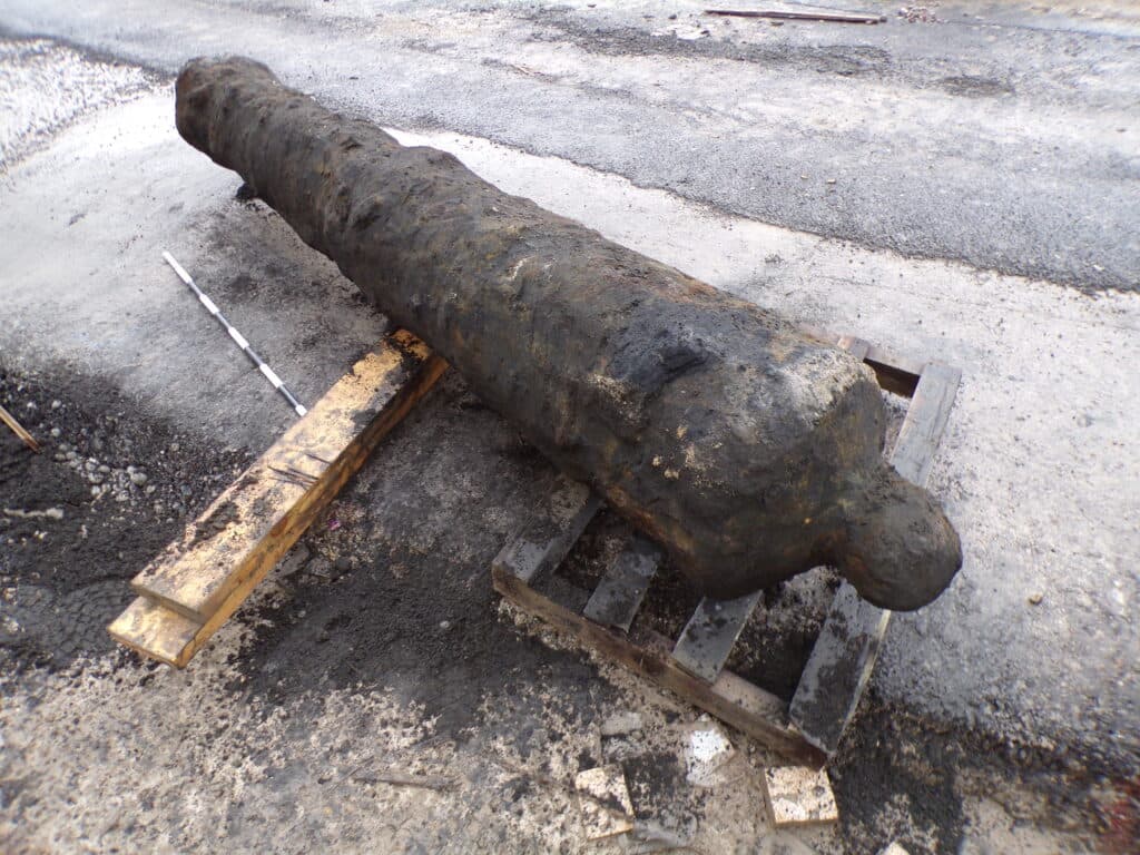 A historic cannon rests on wooden pallets amid construction debris in Queen’s Gardens, Yorkshire, showcasing its weathered surface.