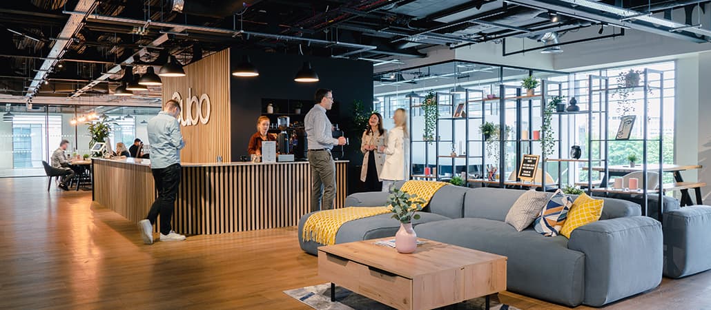 Modern office interior with a welcoming reception, people engaging, and stylish furnishings in a vibrant workspace.