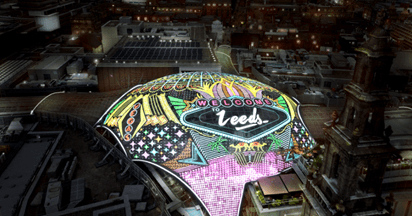 Vibrant illuminated dome reading "Welcome to Leeds" amidst a bustling urban nightscape, showcasing Leeds' architectural charm.