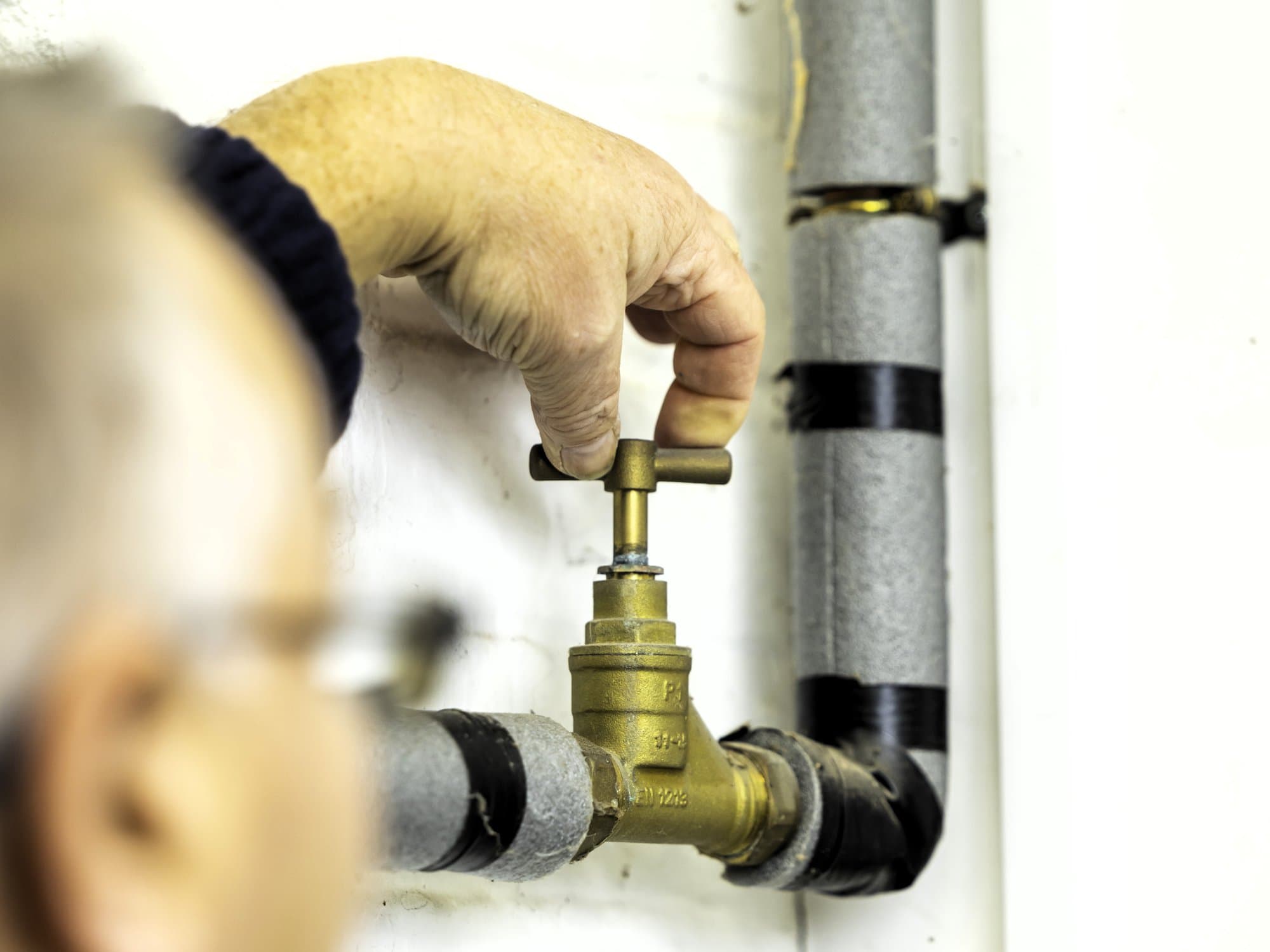 A person adjusts a brass stop tap connected to grey pipes in a well-lit, modern Yorkshire home.