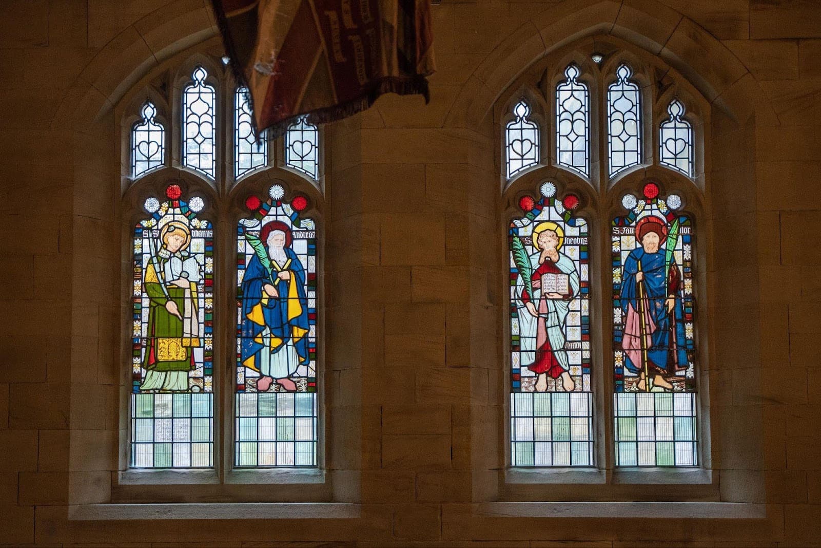 Stained glass windows depicting four figures in vibrant colors, set within a historic Yorkshire church interior.