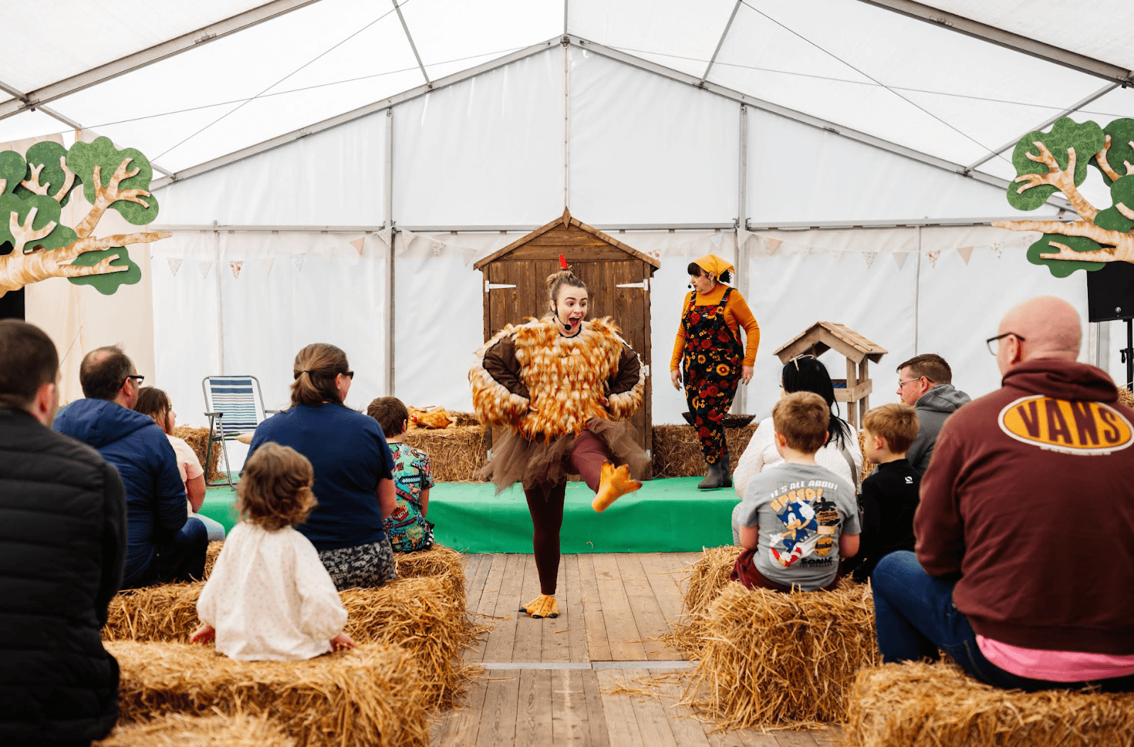 A lively performance in a tent at William's Den, with children and families seated on hay bales, enjoying the show.