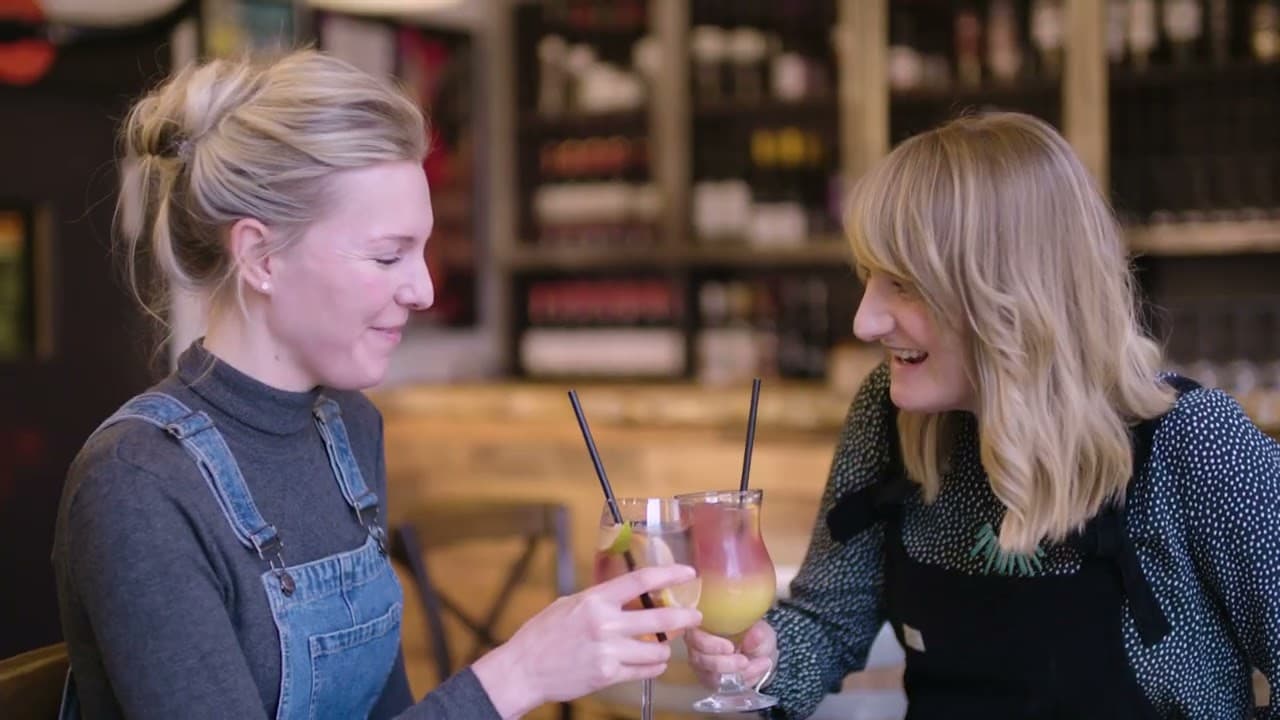 Two women clink glasses filled with colorful cocktails, smiling in a cozy York restaurant setting.