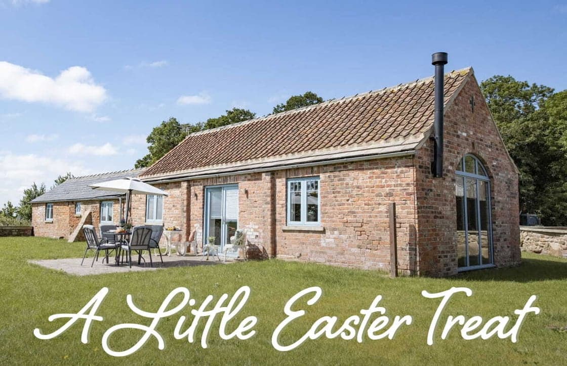 Charming brick cottage with a patio set in lush green countryside, under a bright blue sky, perfect for an Easter getaway.