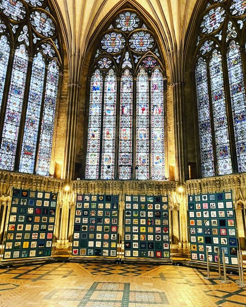 Vibrant quilt displays fill a grand cathedral interior, framed by stunning stained glass windows in Leeds.