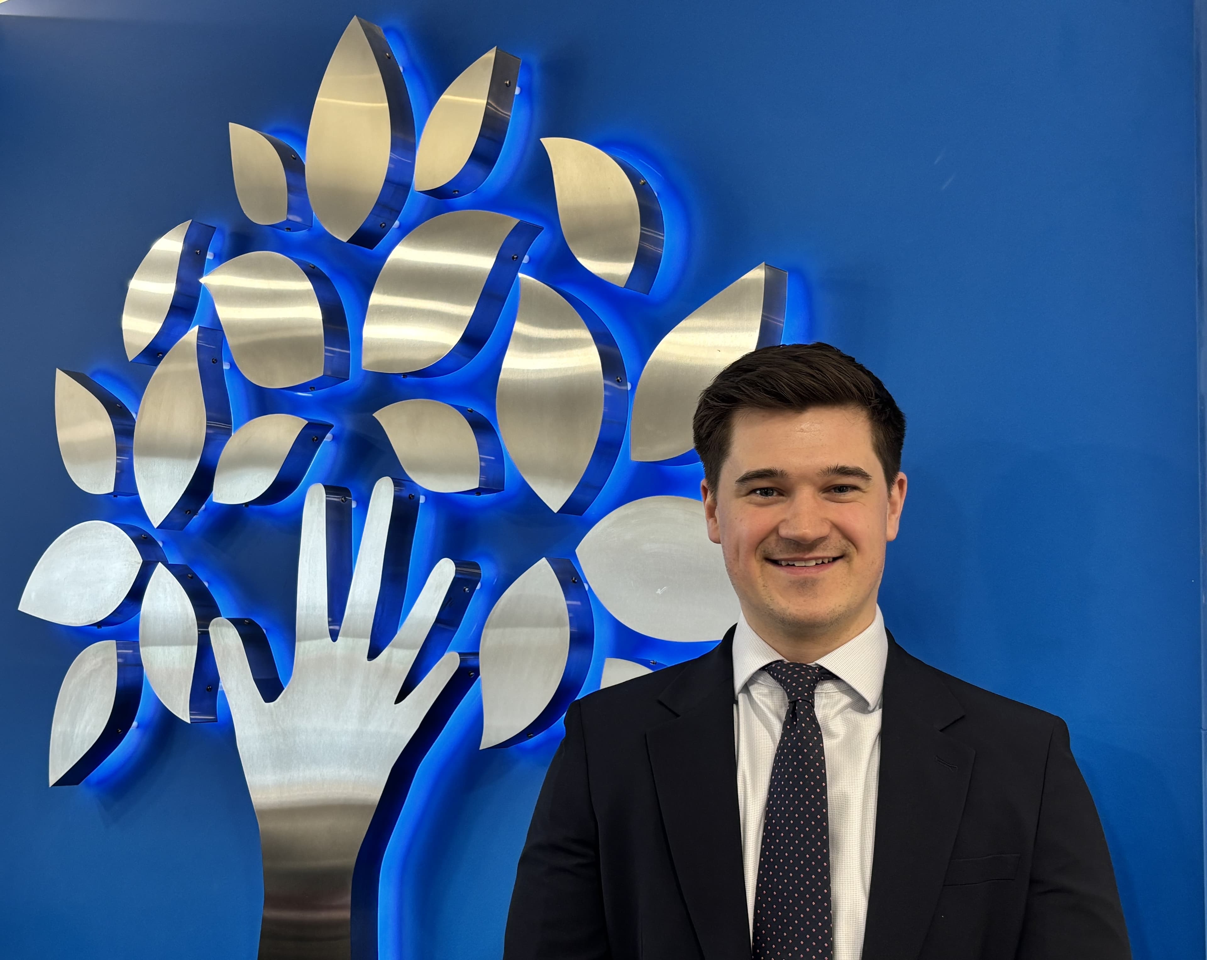 Smiling man in suit standing by modern metal tree sculpture
