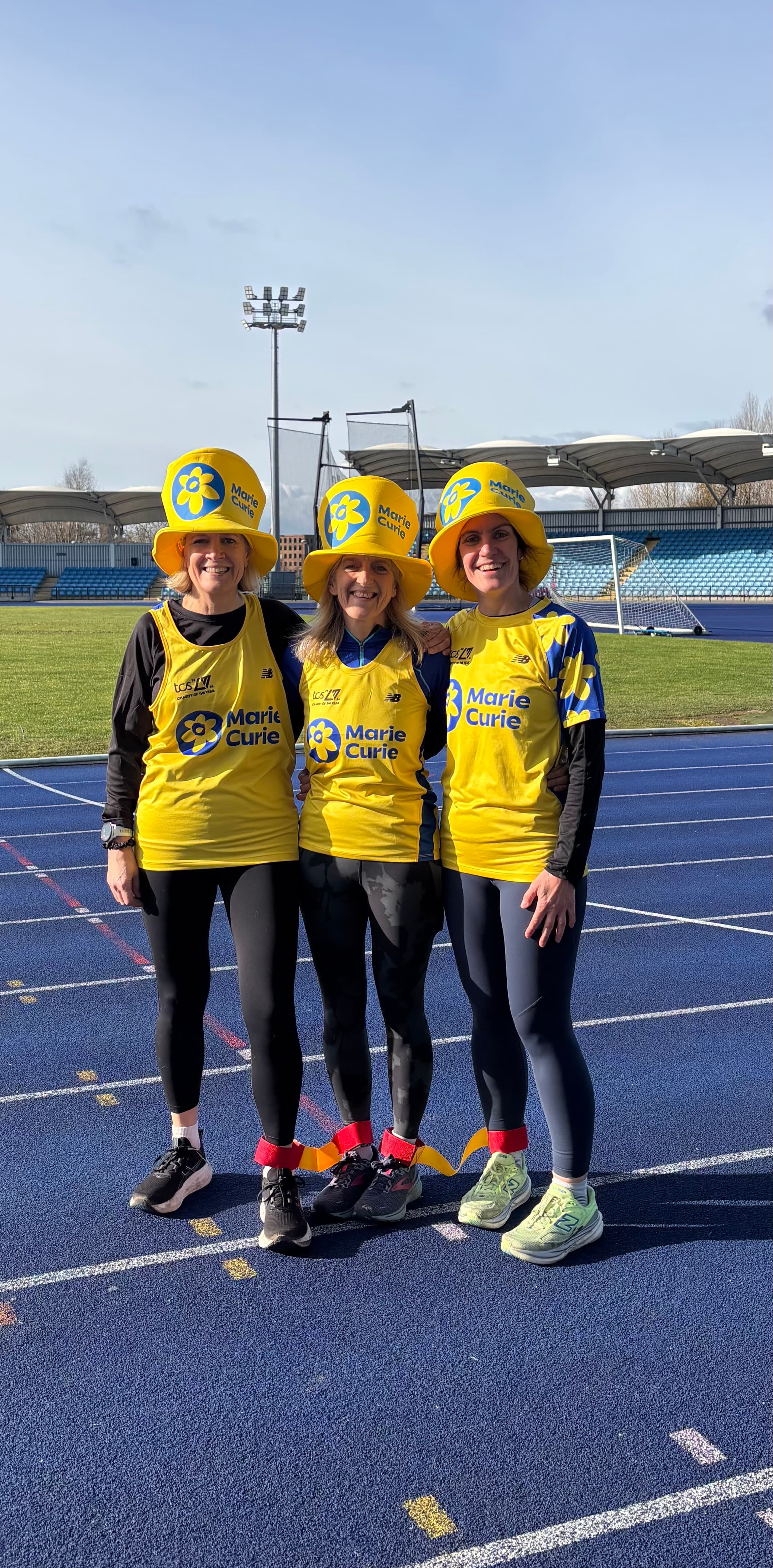 Three people in yellow charity hats and shirts on a running track