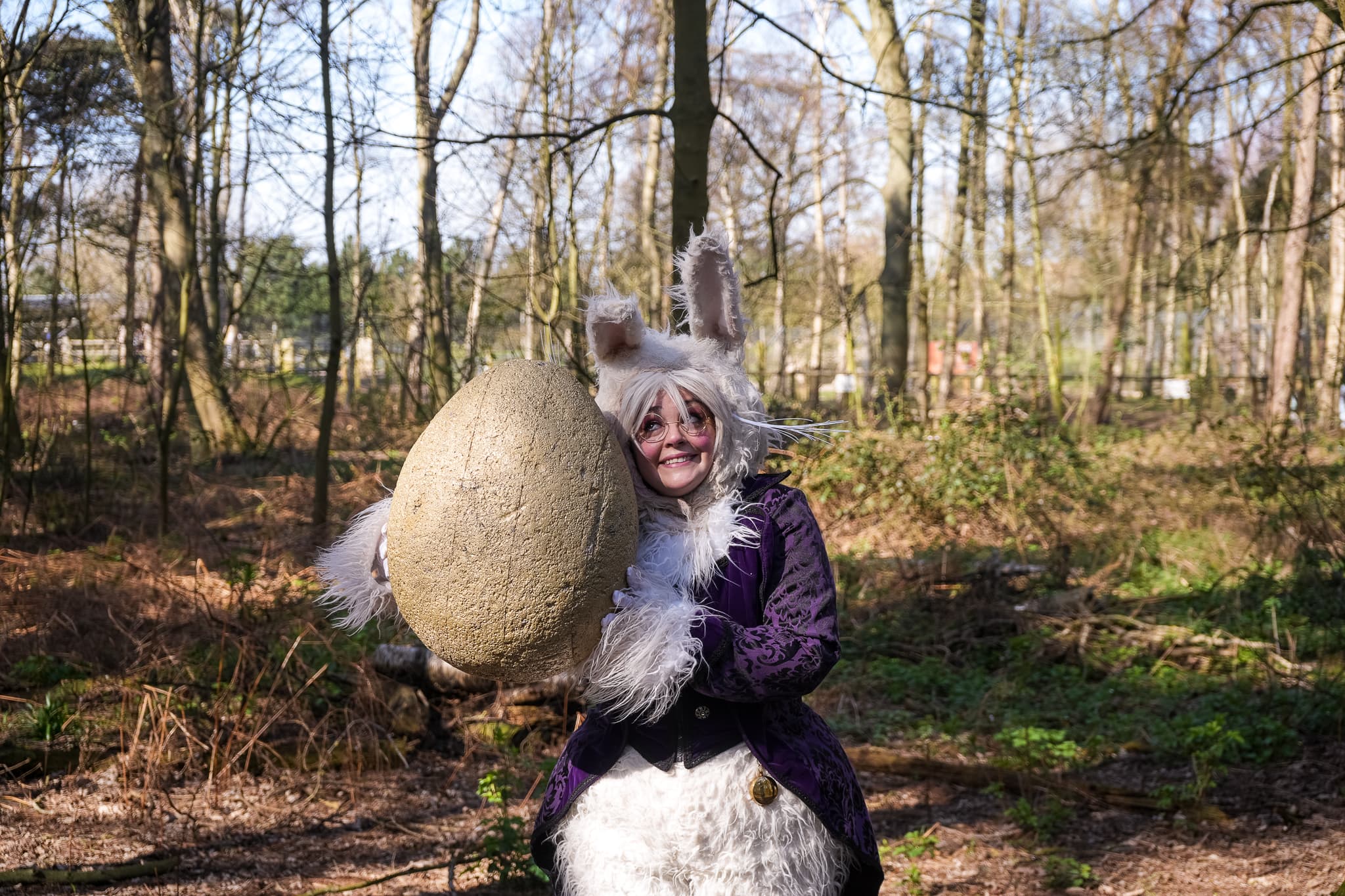 Person in rabbit costume holding large egg in wooded area