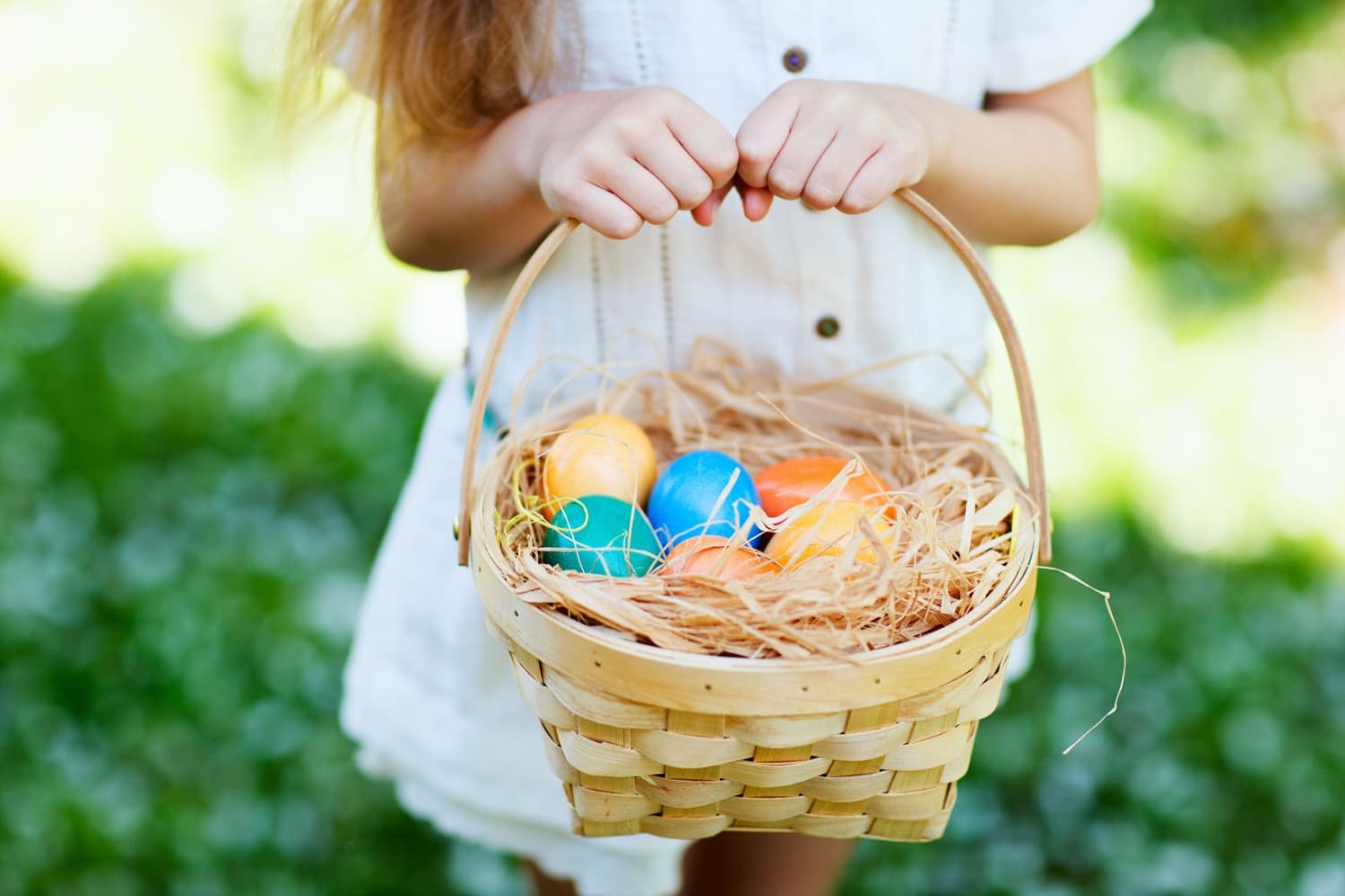 Child holding a basket of colorful eggs in a garden