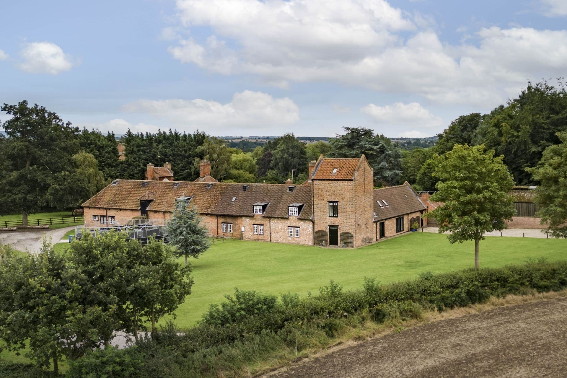 Historic brick farmhouse with red roof surrounded by trees