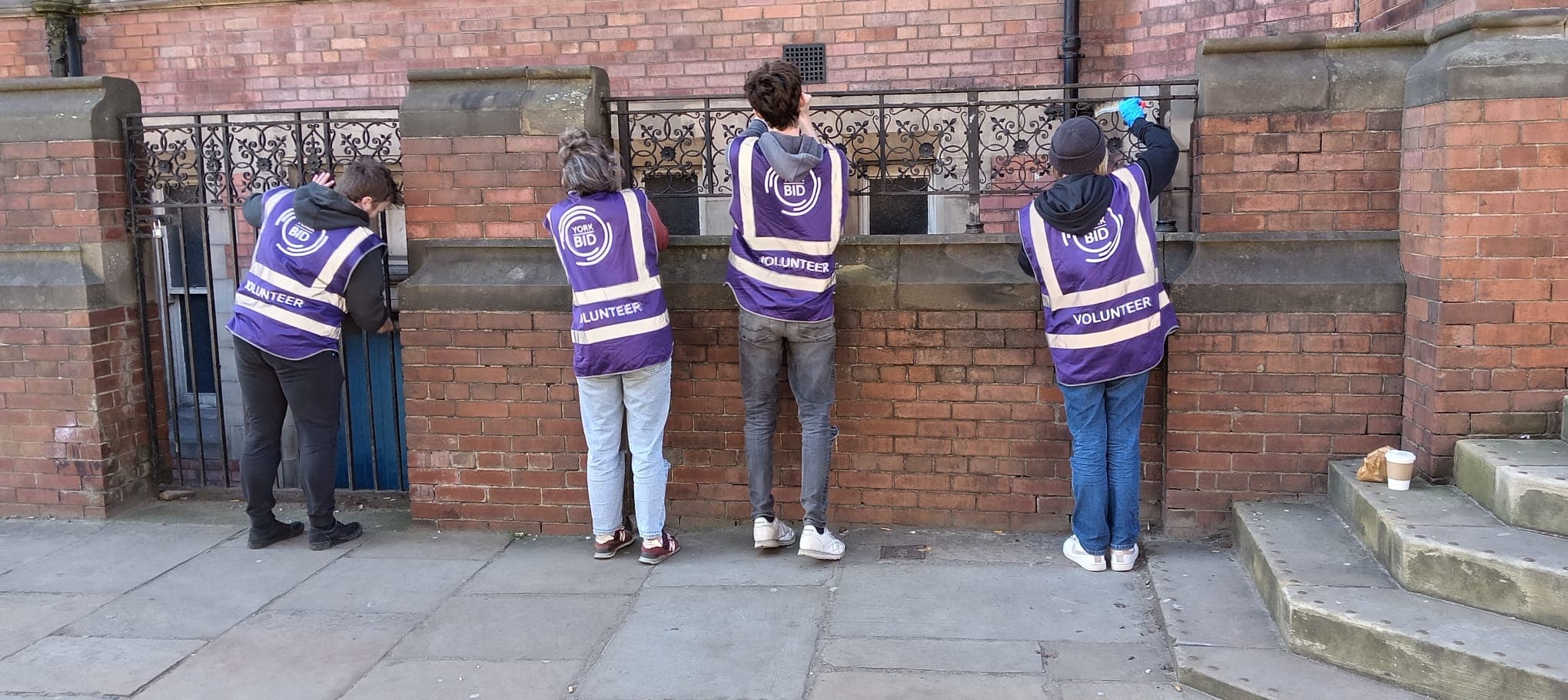 Volunteers in purple vests painting red brick wall in city