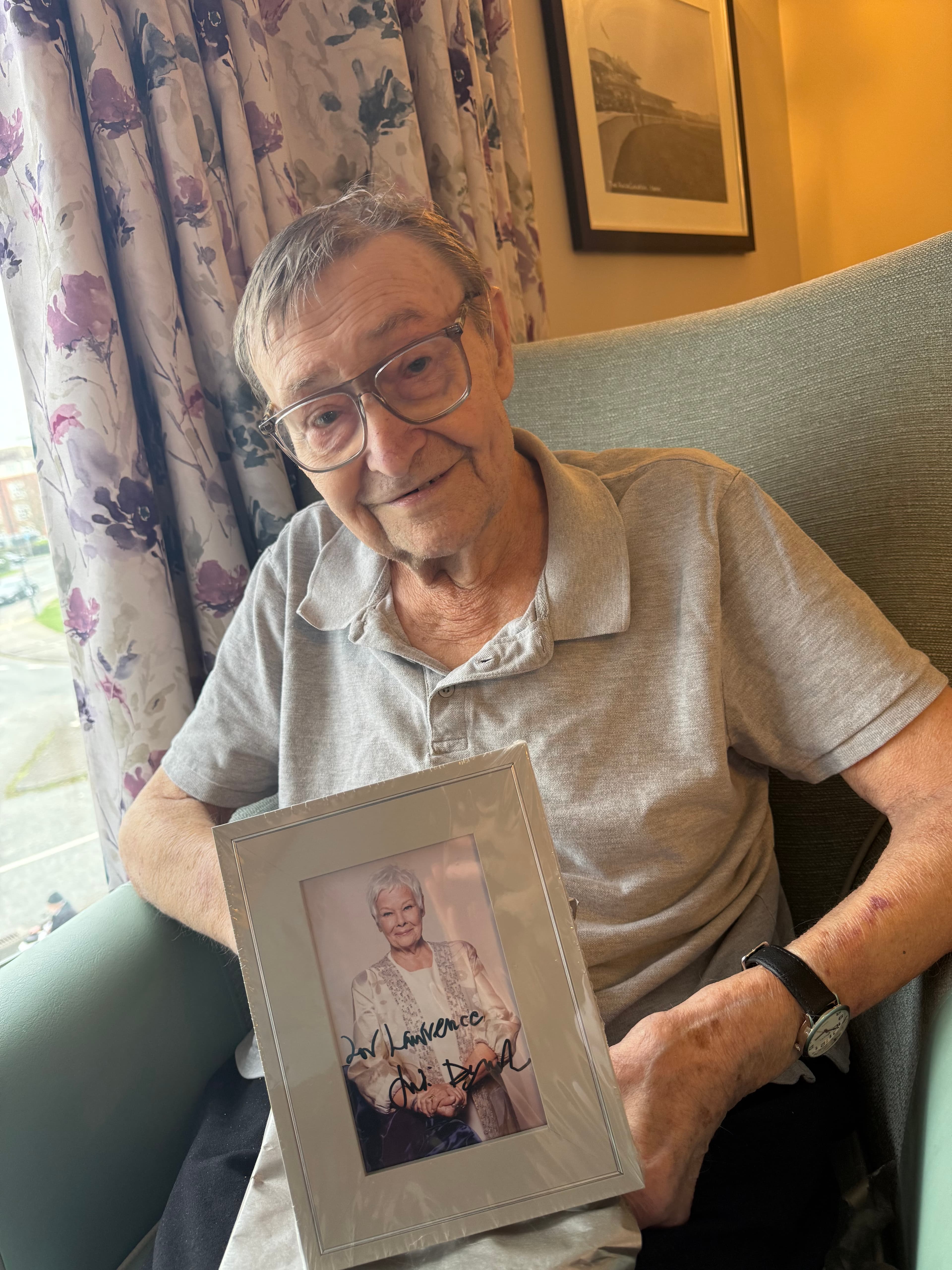 Elderly man smiling in armchair holding signed portrait