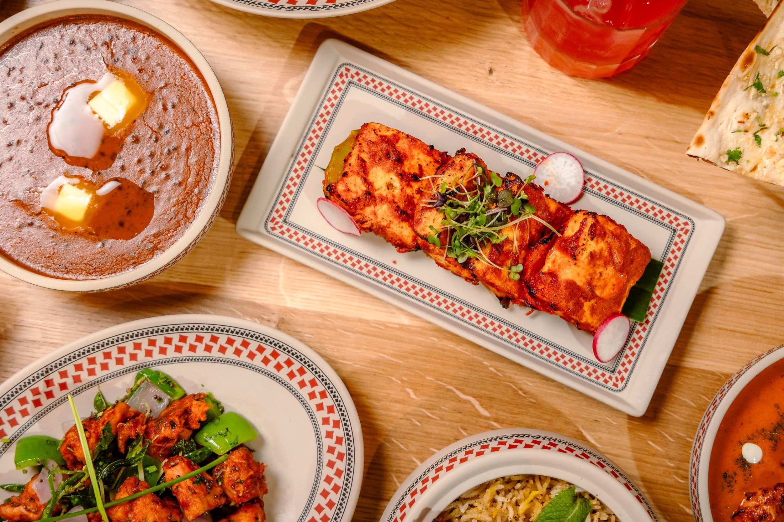 Assorted Indian dishes on wooden table with naan bread