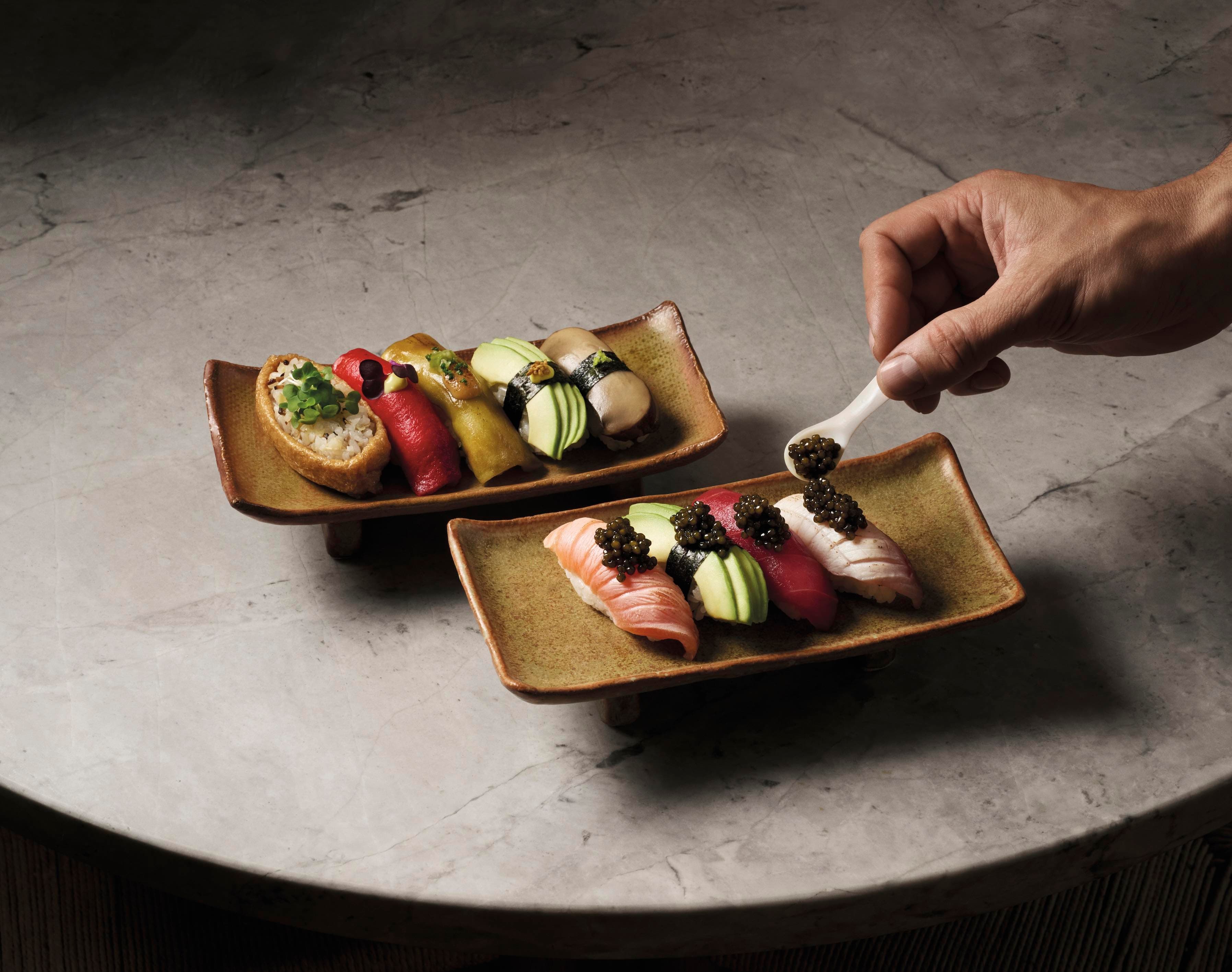 Hand placing caviar on assorted sushi on ceramic plates